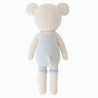 Knitted teddy bear wearing light blue overalls on a white background