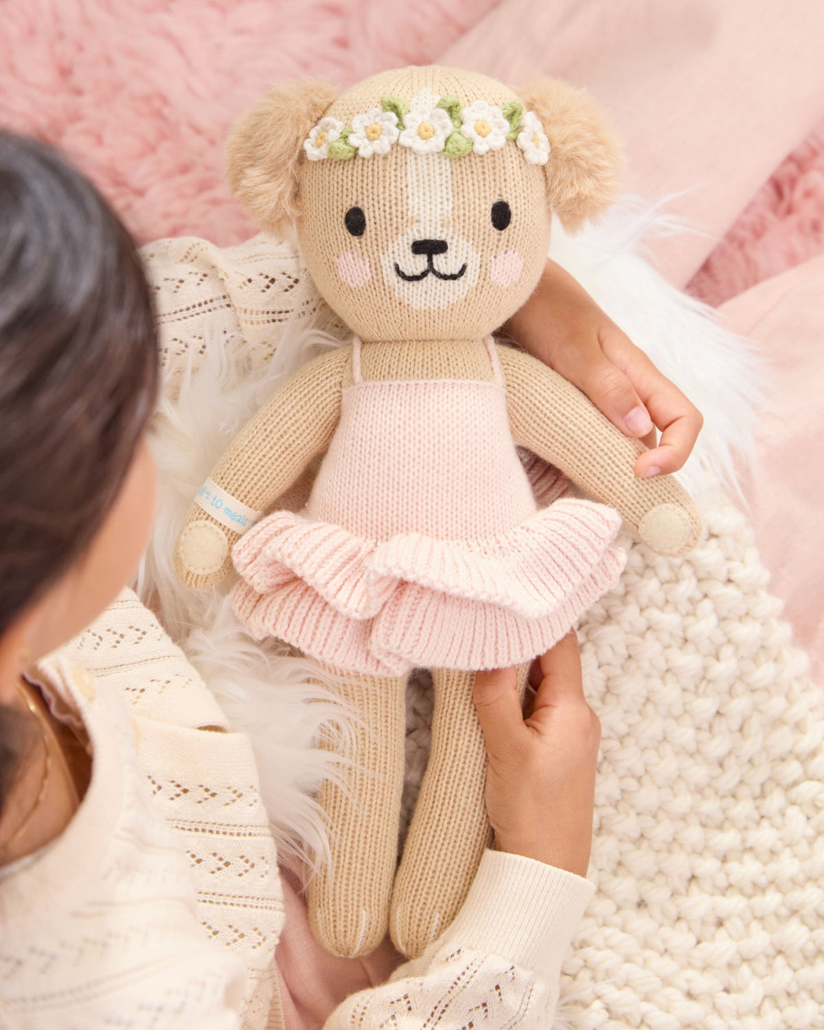 Knitted teddy bear in a pink dress held by a person against a soft pink background