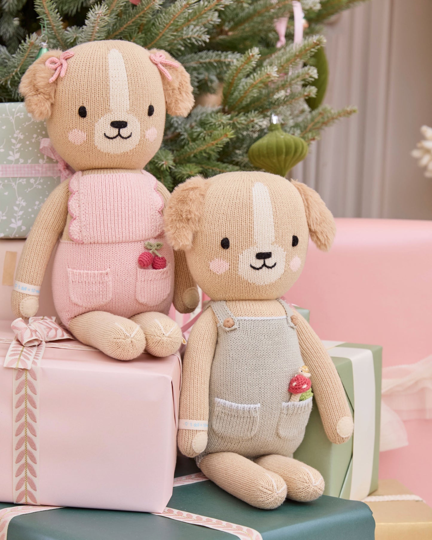 Two knitted teddy bears sitting on presents with a Christmas tree in the background