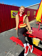 Person in a hot dog costume sitting on a red bench with a red fence and colorful decorations in the background.