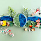 Playdough with green and blue colors, surrounded by small toys and items on a light green background