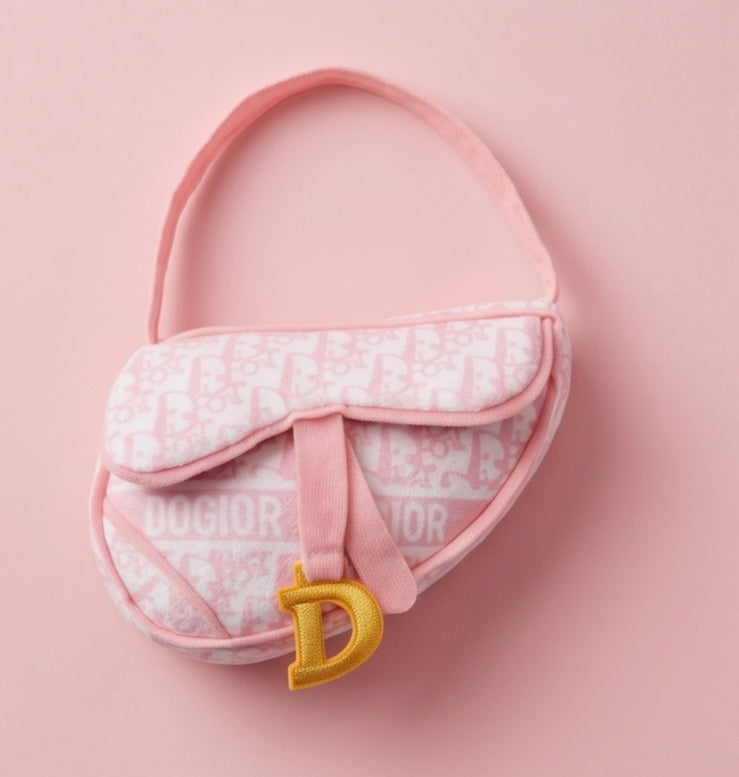 A pink Christian Dior Dandy bag with a white monogram pattern and a gold 'D' charm, displayed on a solid pink background.