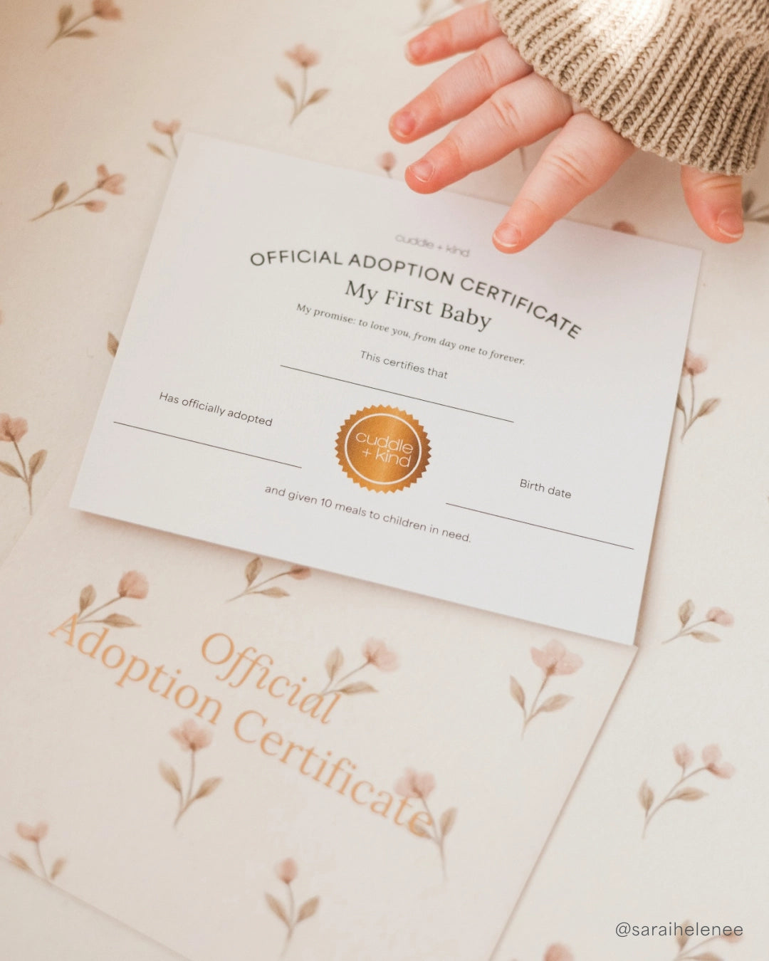 Hand holding an 'Official Adoption Certificate' on a floral-patterned background