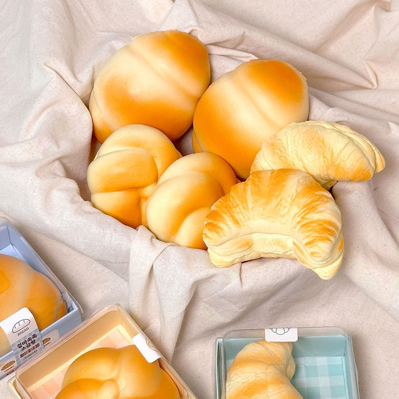 Assorted bread rolls including buns and croissants on a light fabric background