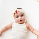 Baby wearing a white headband with a strawberry design on a plain background