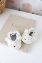 White baby booties with gray accents on a beige blanket labeled 'baby'.