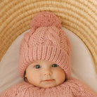 Baby wearing a pink knitted outfit with a matching hat in a wicker basket.