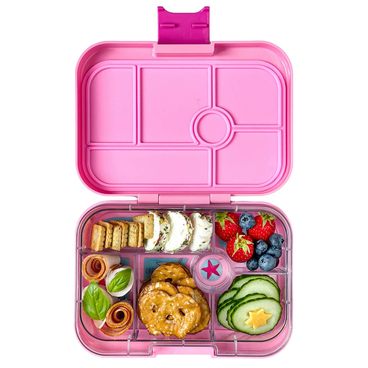 Pink bento box with compartments filled with snacks and fruits on a white background
