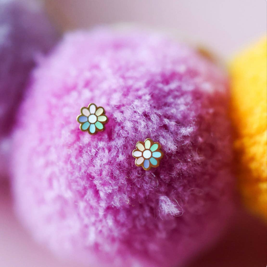 Flower-shaped earrings on a soft, multicolored fabric background