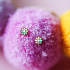 Flower-shaped earrings on a soft, multicolored fabric background