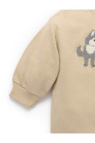 Close-up of a beige long-sleeve knit top with a gray and white dog patch on the chest, showing the ribbed cuff and part of the body against a white background.