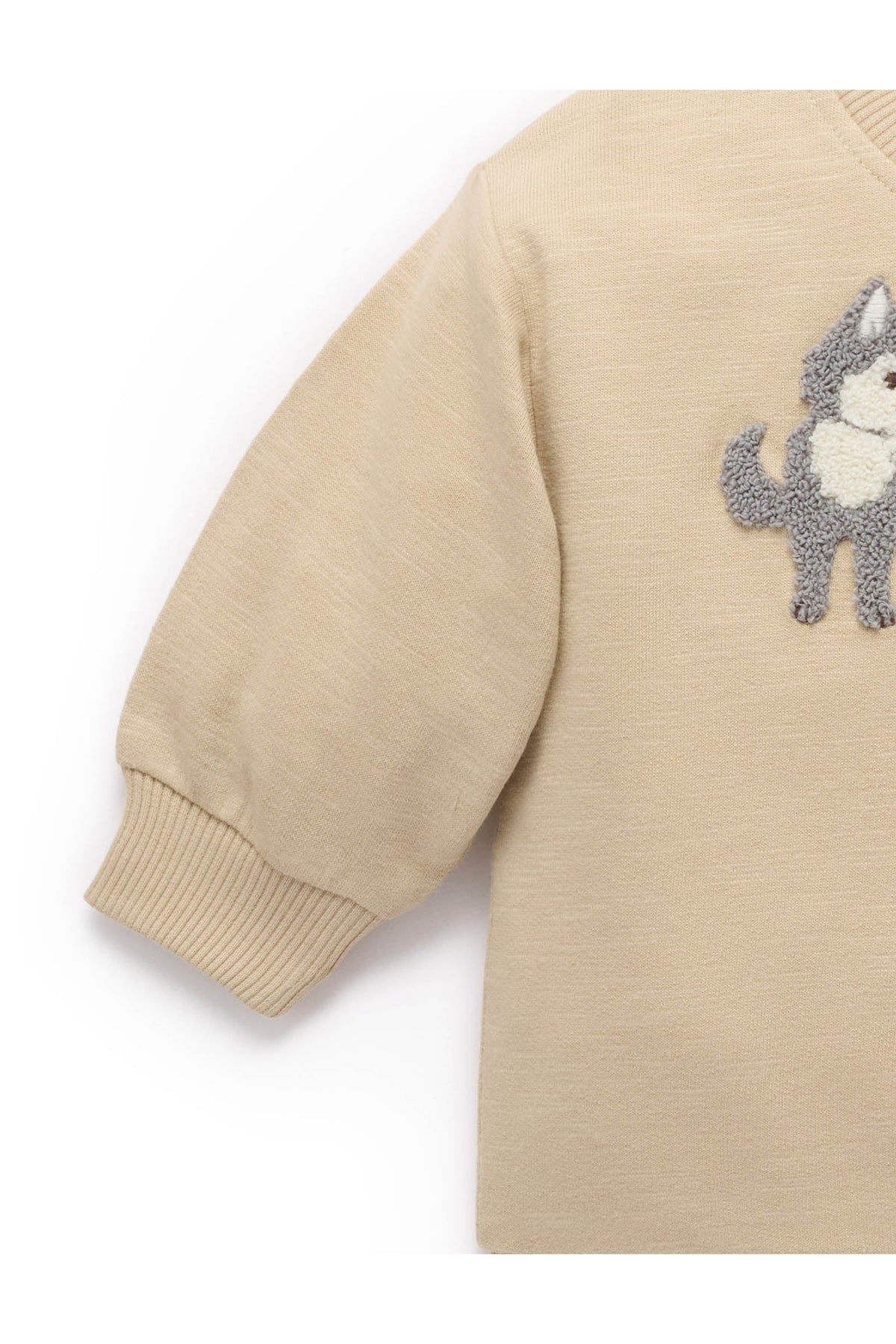 Close-up of a beige long-sleeve knit top with a gray and white dog patch on the chest, showing the ribbed cuff and part of the body against a white background.