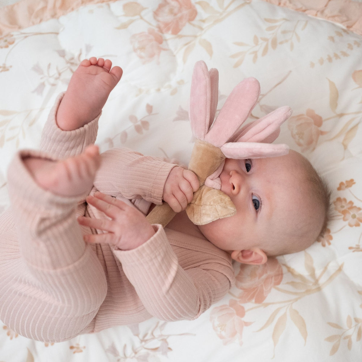 Baby lying on a floral blanket with a pink bunny toy