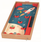 A children's wooden space-themed marbles game in a cardboard box, featuring a blue starry board with a rocket, planets, scoring holes, and red corner bumpers.