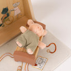 Small plush pig in a green outfit on a wooden toy with a white background