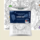 A packaged reusable silicone sensory mat by Hey Doodle, labeled 'Alphabet Soup,' shown in front of a partially visible uncolored coloring page. The package is white with a dark blue front label and includes small color swatches indicating included colors.