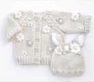 Knitted baby cardigan and booties with floral embellishments on a white background