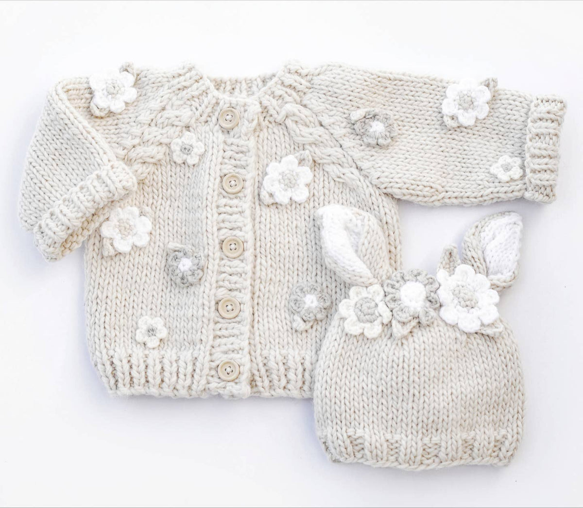 Knitted baby cardigan and booties with floral embellishments on a white background