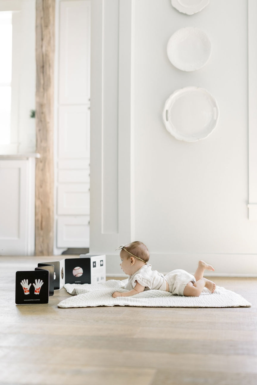 Baby lying on a white rug in a minimalistic room with white walls and wooden floor.