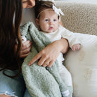 Woman holding a baby wrapped in a green blanket on a couch