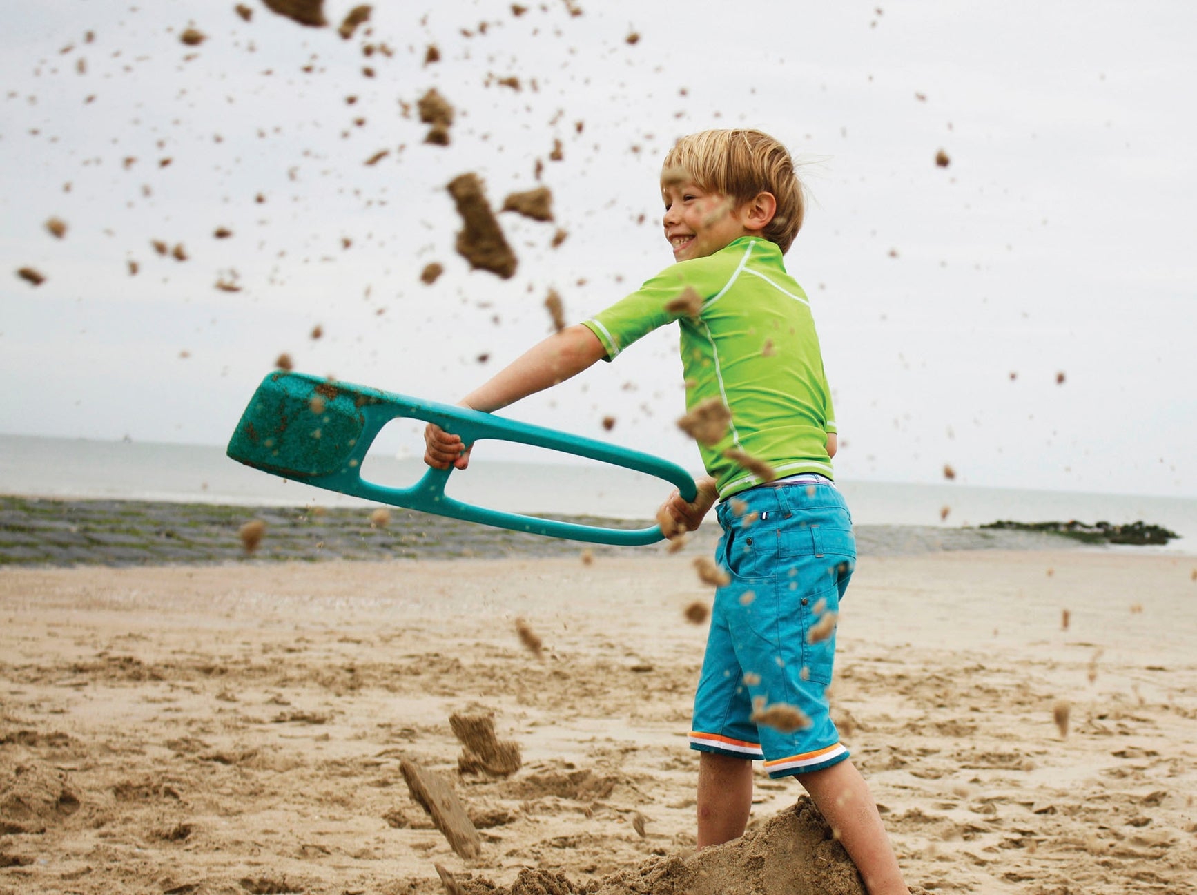 Child playing on a sandy beach with a sandcastle shovel