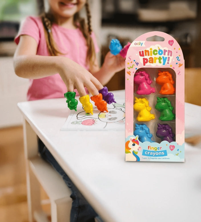 Child playing with colorful unicorn-shaped crayons next to their packaging on a table.