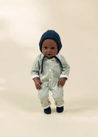 Baby in a striped outfit and blue hat standing on a beige background
