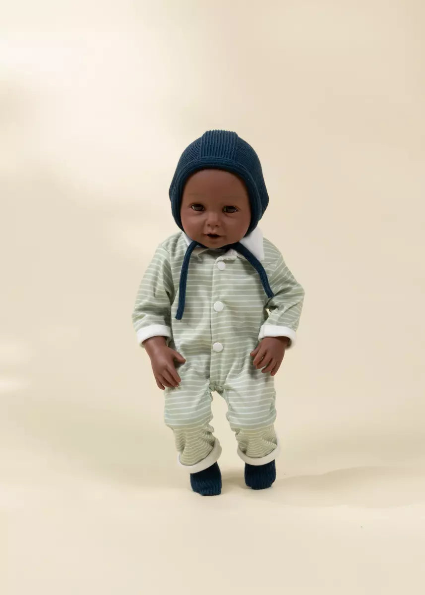 Baby in a striped outfit and blue hat standing on a beige background