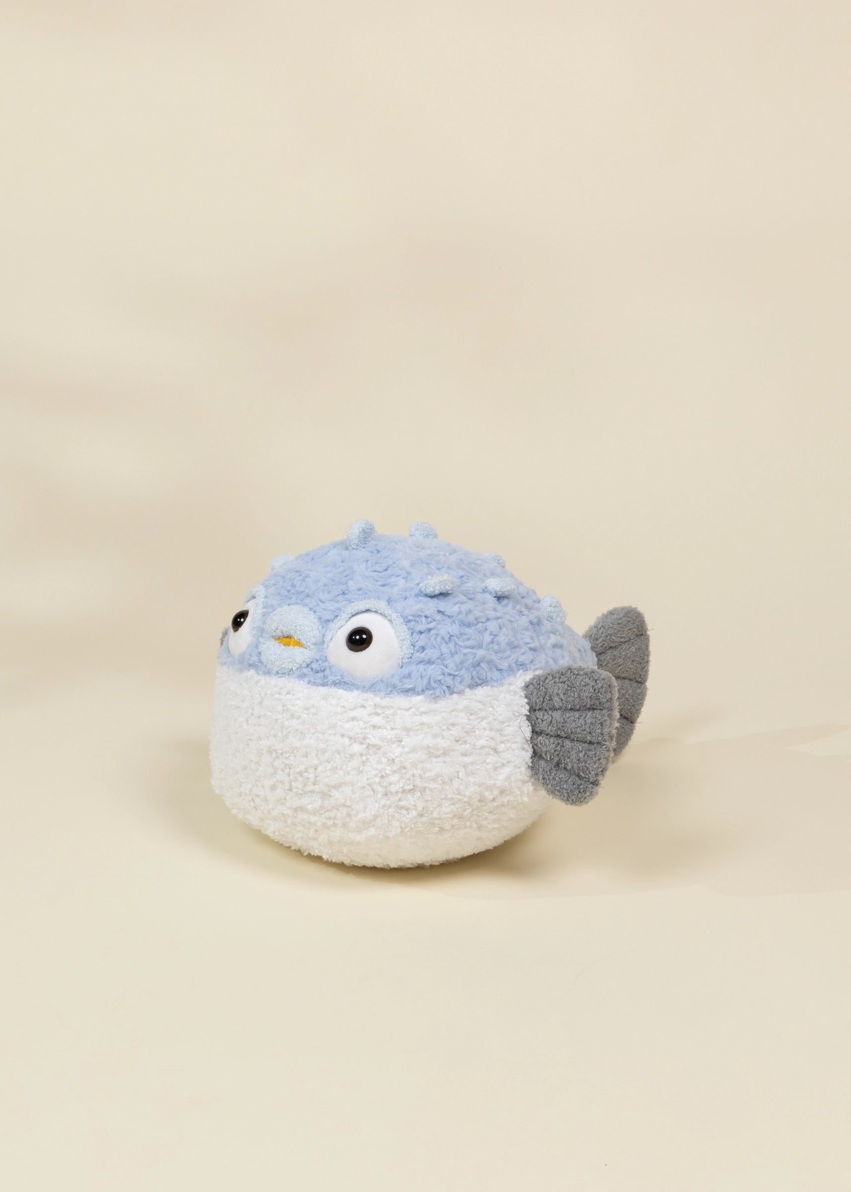 Stuffed toy resembling a bird with a blue head and gray wings on a beige background