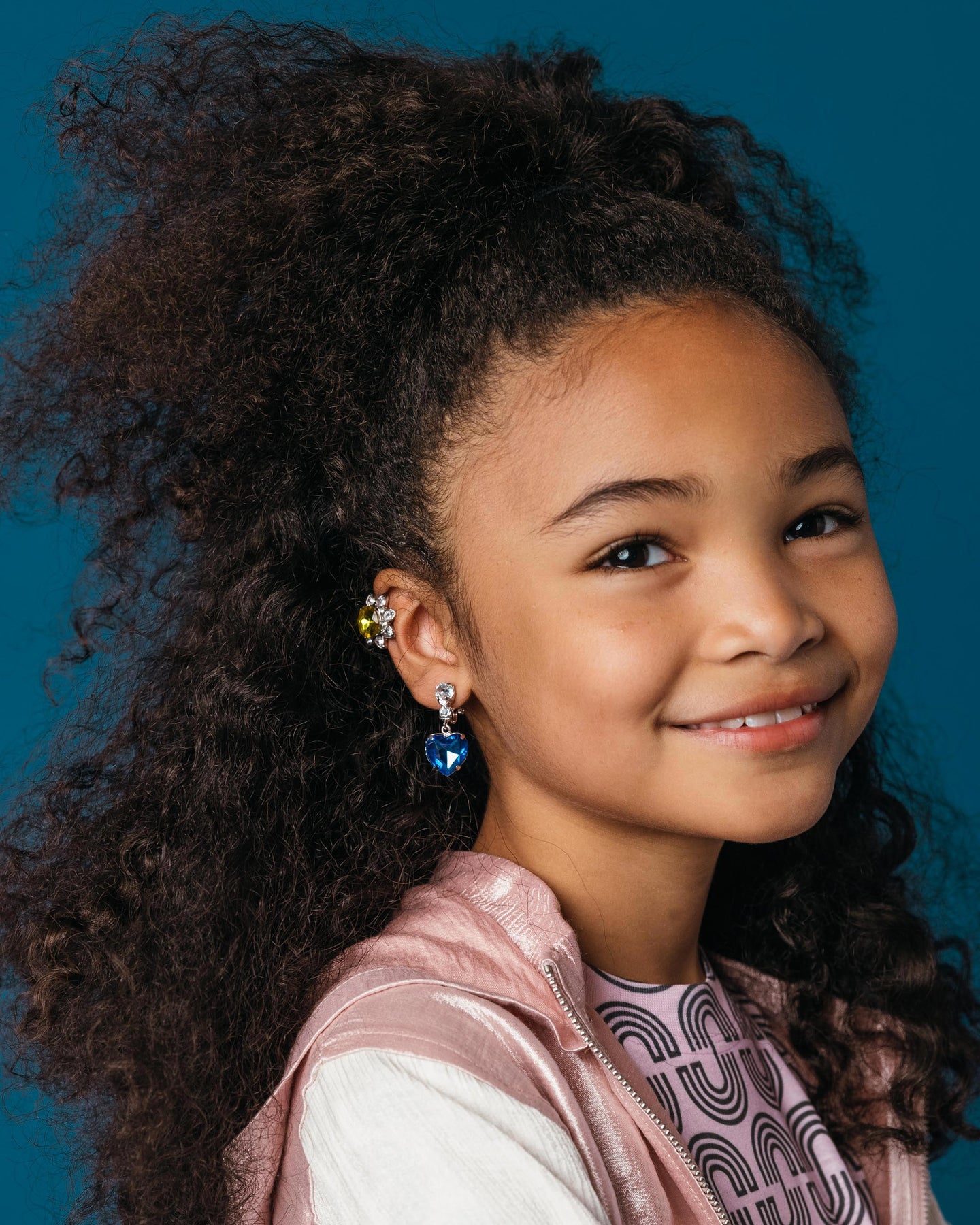 Young girl with styled hair wearing earrings against a blue background