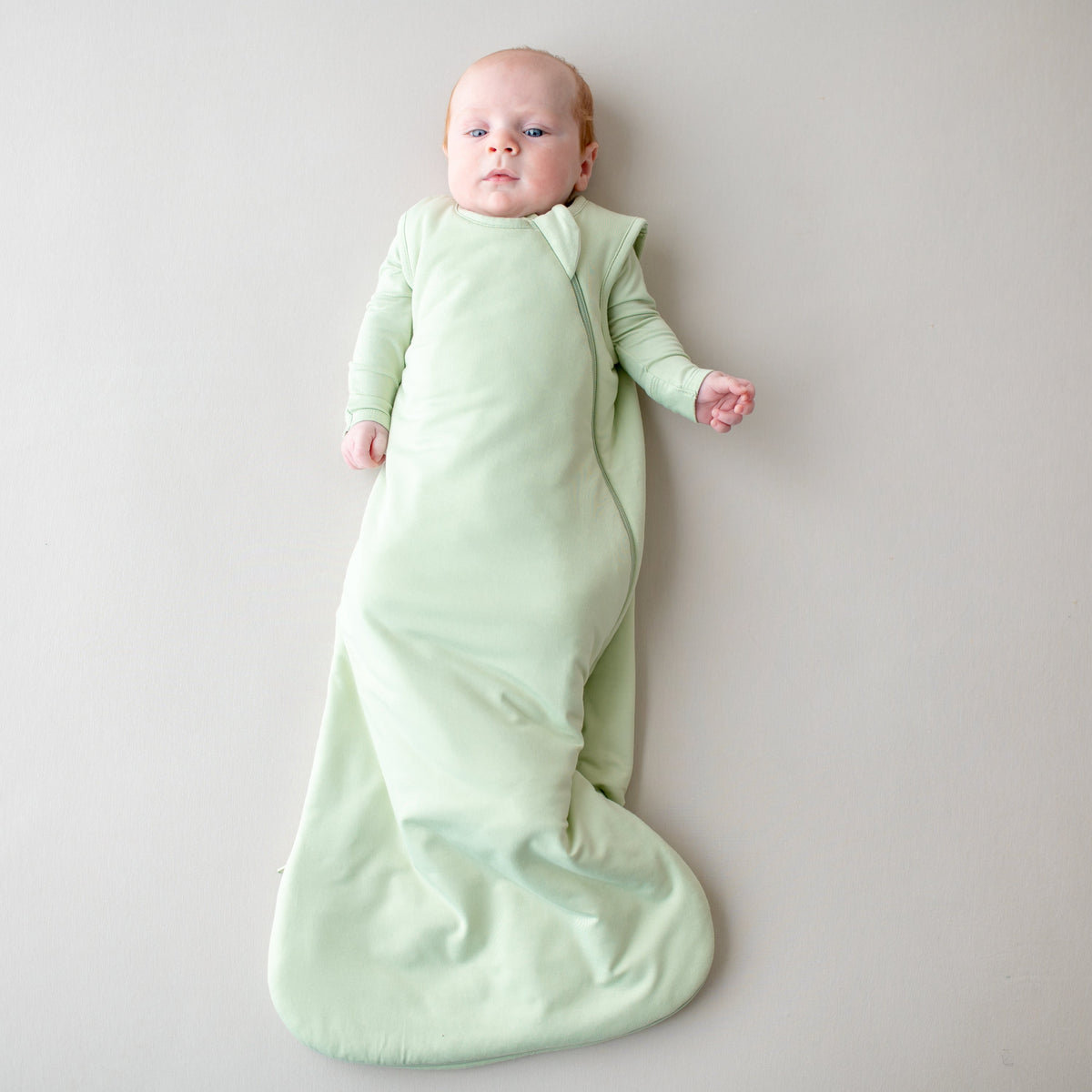 Baby wrapped in a light green swaddle on a plain background