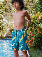 Child wearing blue swim shorts with peacock pattern by a poolside