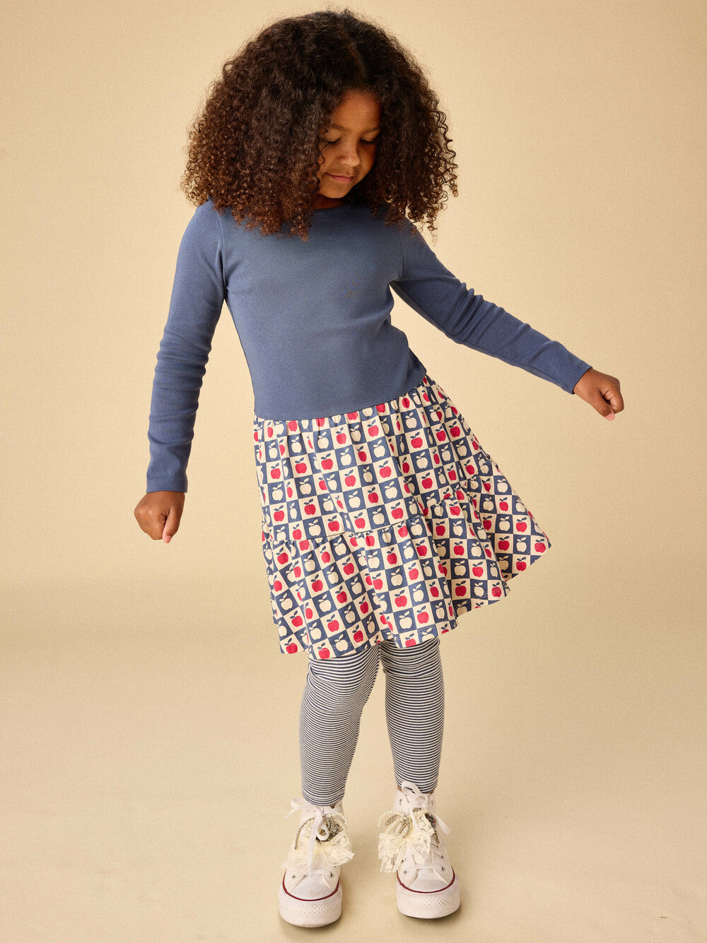 Child wearing a blue top and patterned skirt on a beige background