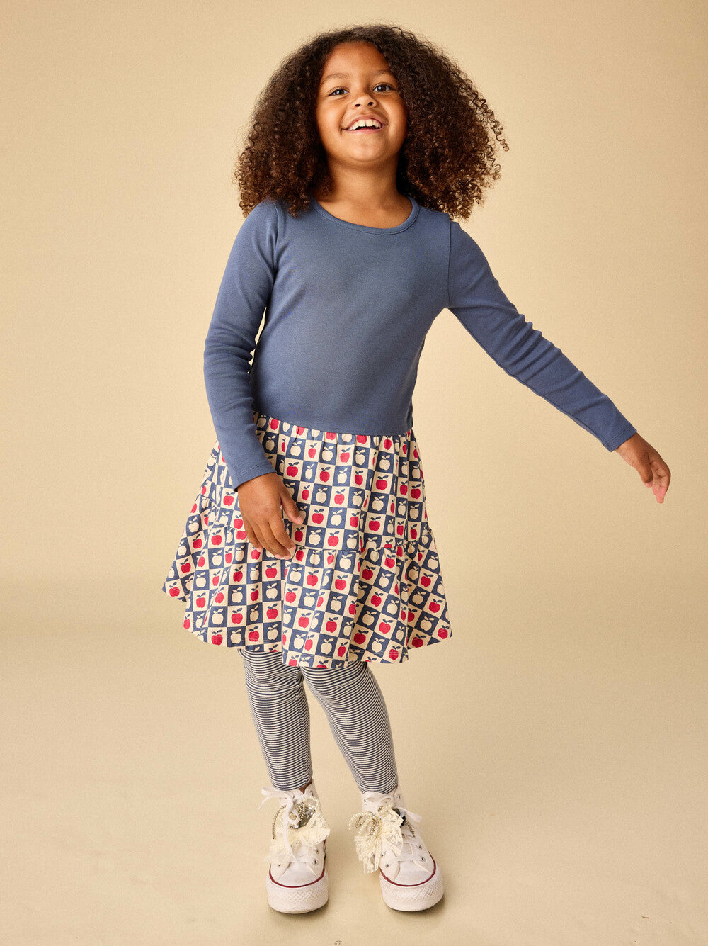 Child wearing a blue long-sleeve top and patterned skirt on a beige background