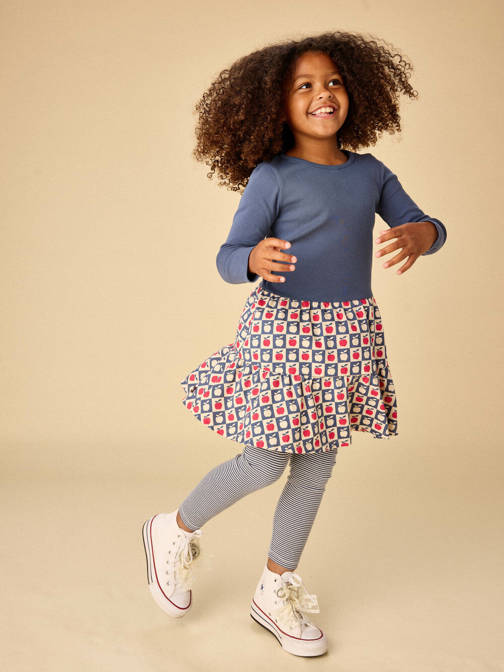 Child wearing a blue top and patterned skirt on a beige background