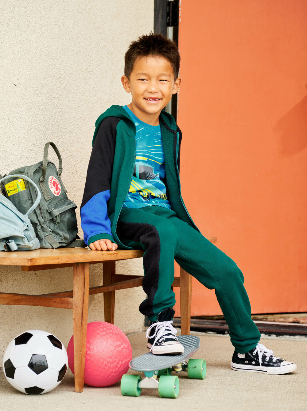 Child sitting on a chair with sports equipment and a skateboard