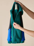 Person holding a green and blue jacket with a beige background