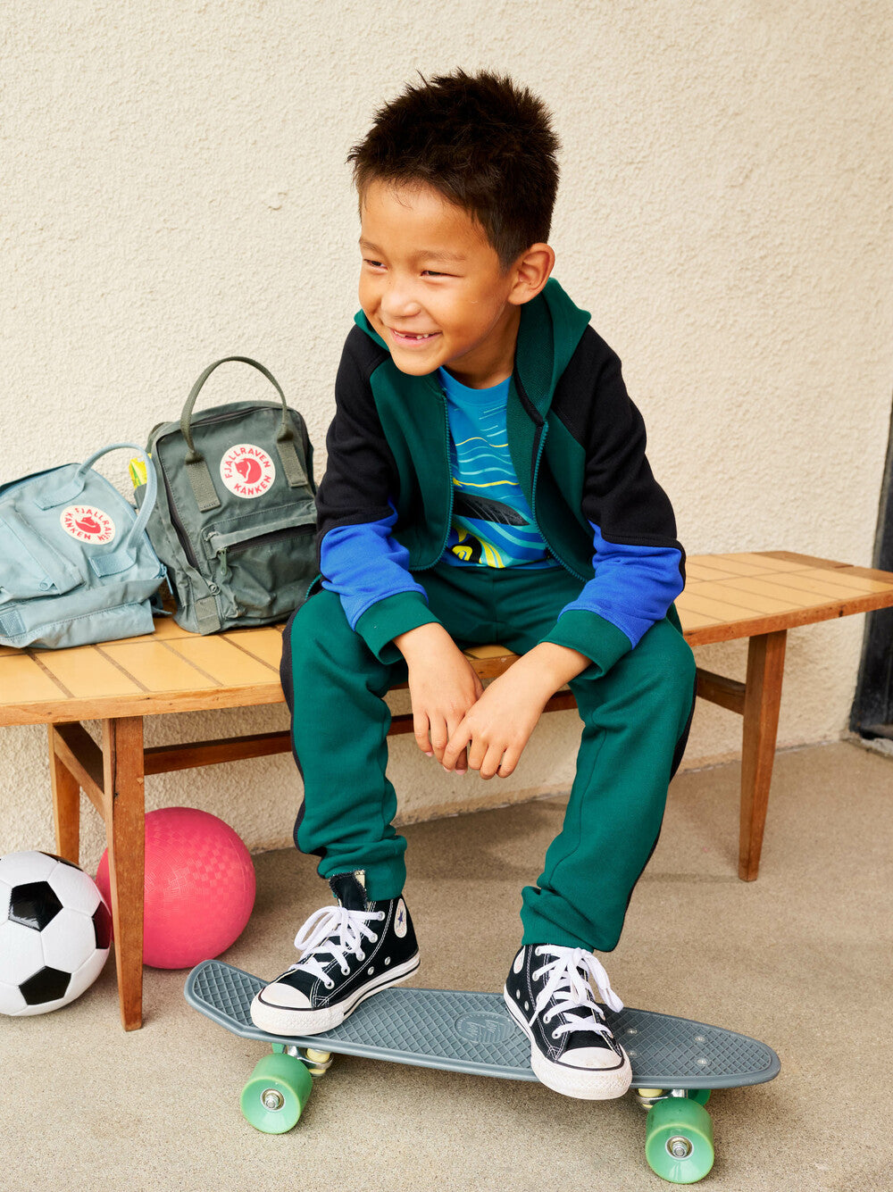 Child sitting on a skateboard with sports equipment in the background