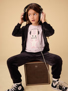 Child wearing headphones sitting on a speaker with a neutral background