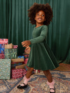 Young girl in a green dress standing in front of Christmas presents with a green curtain background