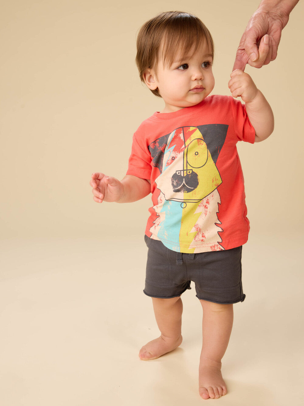 Baby wearing a colorful t-shirt with a cartoon design on a beige background
