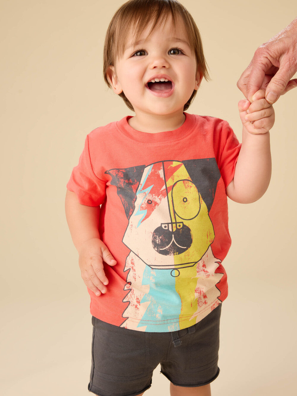 Child wearing a red t-shirt with a colorful dog graphic on a beige background