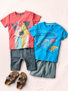 Two children's t-shirts with graphic designs and shorts, paired with sandals on a light background.