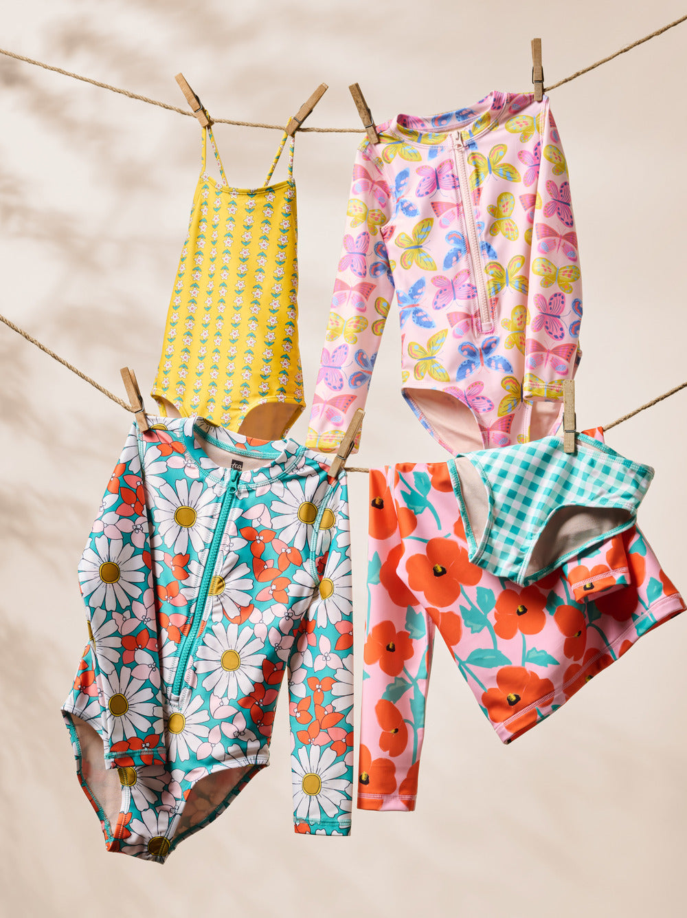 Colorful children's swimsuits and clothing hanging on a clothesline against a beige background.