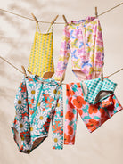 Colorful children's swimsuits and clothing hanging on a clothesline against a beige background.