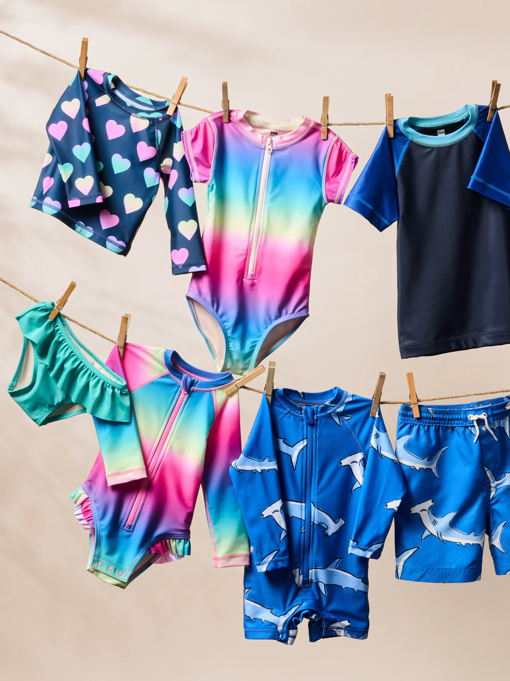 Colorful children's swimwear hanging on a clothesline against a beige background