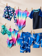 Colorful children's swimwear hanging on a clothesline against a beige background