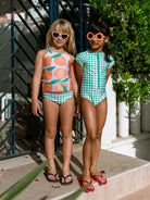 Two children wearing colorful swimsuits and sunglasses outdoors.