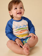 Child wearing a colorful long-sleeve shirt with fish design on a beige background