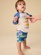 Child wearing a colorful shirt and shorts set with fish design on a beige background